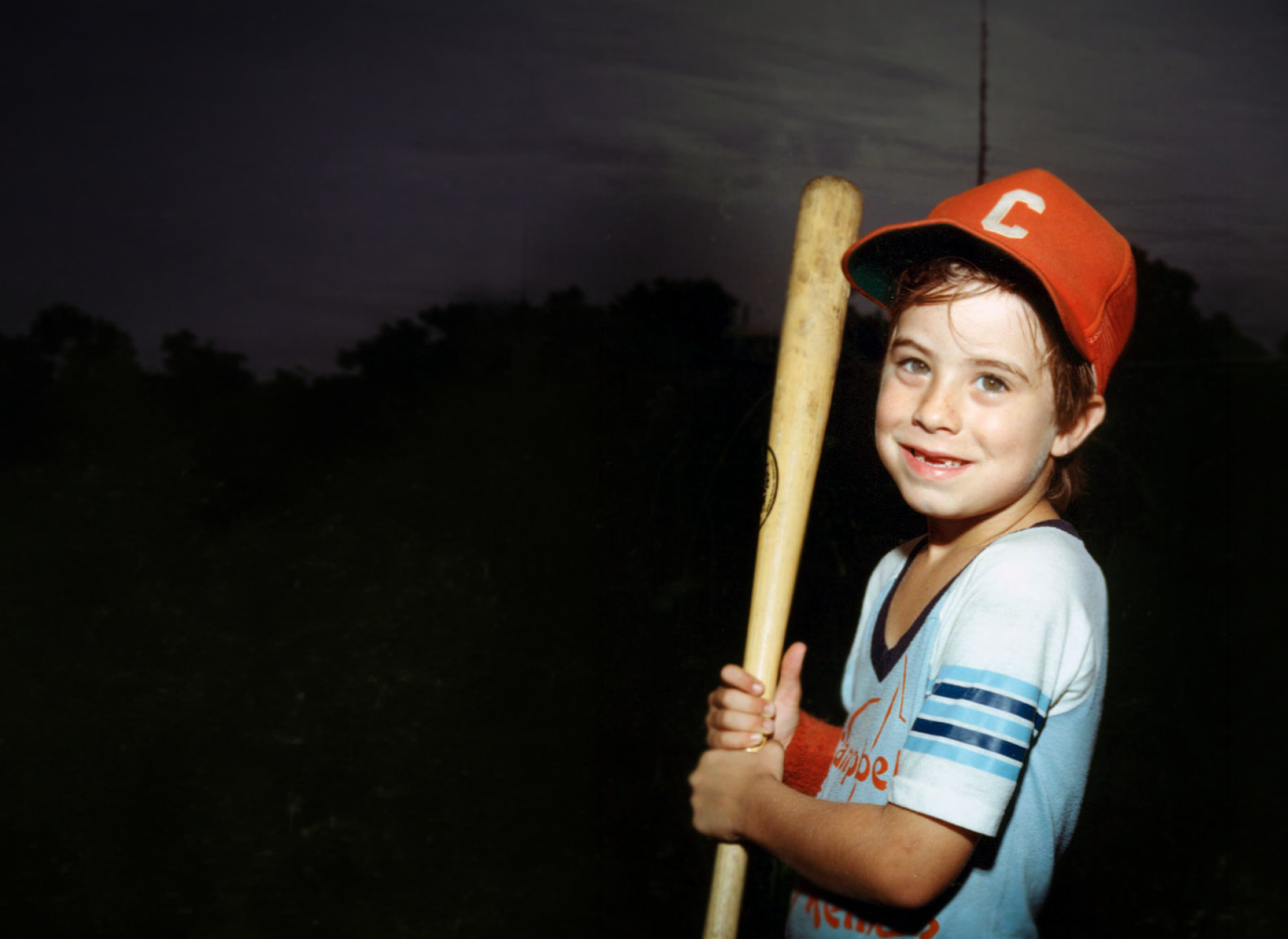 adam smiling, holding baseball bat and wearing red hat