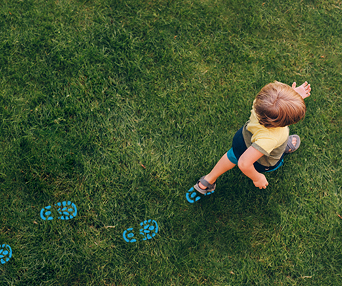 blonde boy walks in grass with blue shoe prints footprints